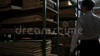 一个穿着白色衬衫的少年走在<strong>图书馆</strong>的<strong>书架</strong>之间，<strong>书架</strong>上放着旧文件，寻找文学作品。 地下室存档